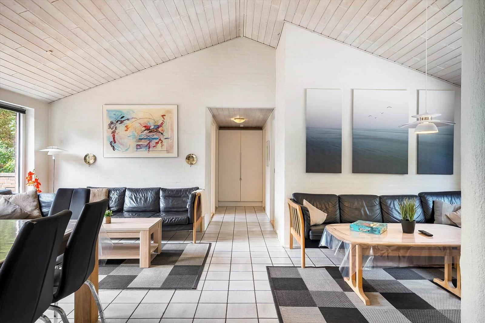 Wohnbereich mit zwei Sofas, Holztischen und Wandbildern unter einer Holzdecke.