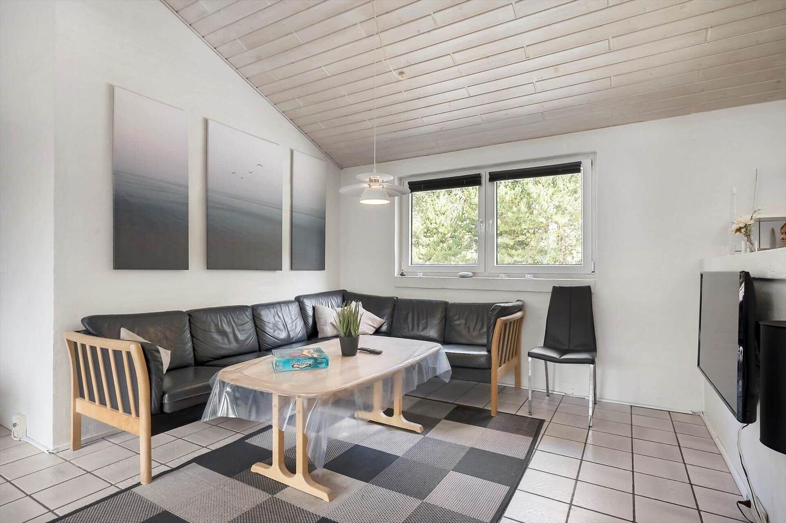 Wohnzimmer mit Sofa, Tisch und Fenster. Decke aus Holz, Wandbilder und Teppich.