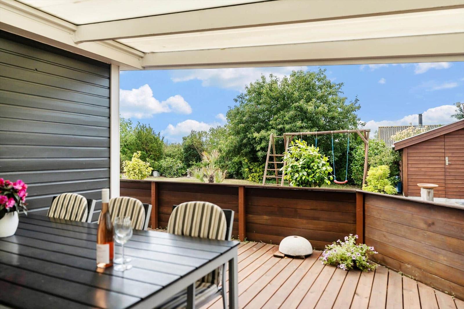 Terrasse mit Tisch, Stühlen und Blick auf Spielplatz und Garten.