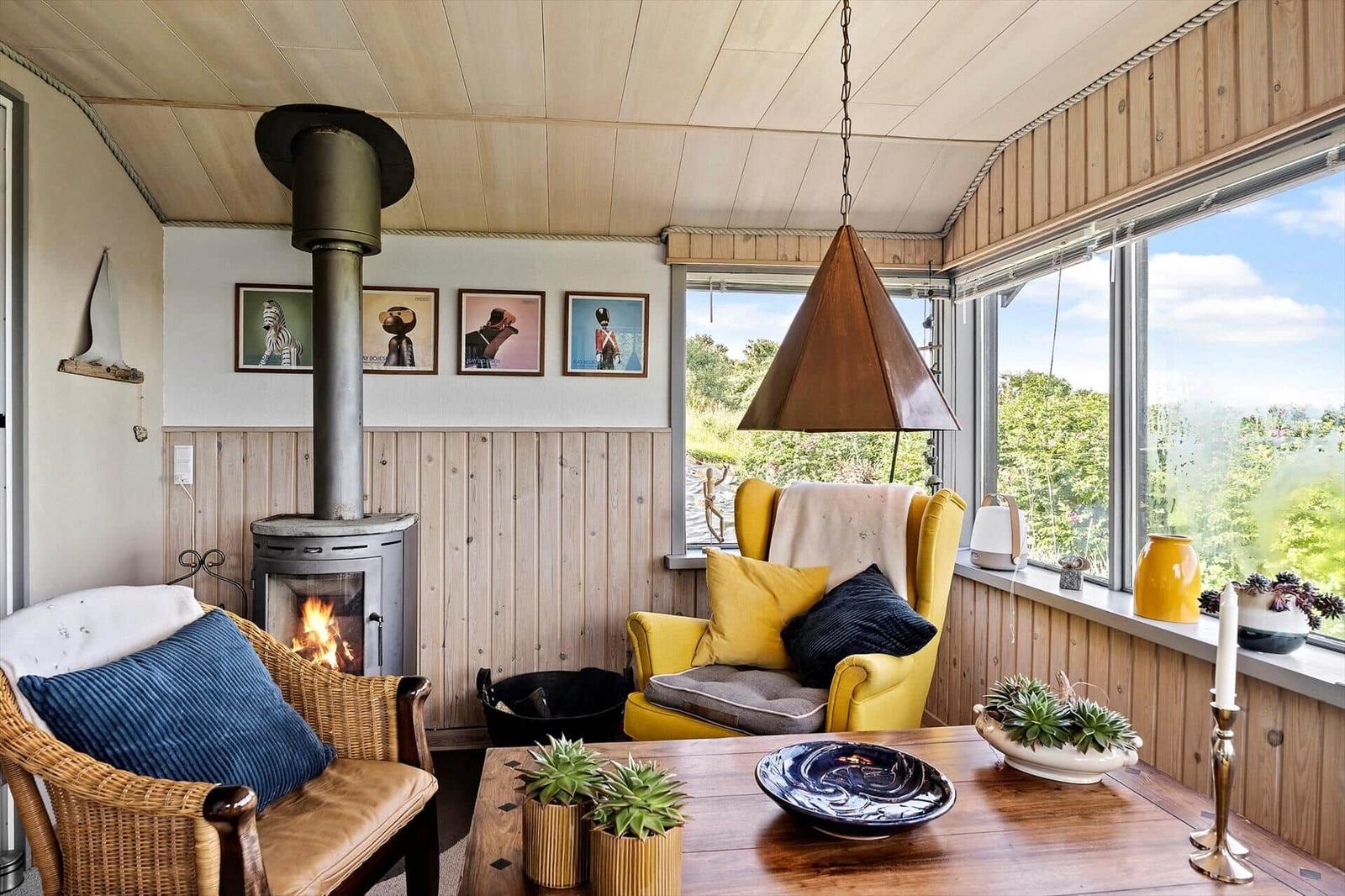 Room with fireplace, yellow armchair, and large window with view of the landscape.