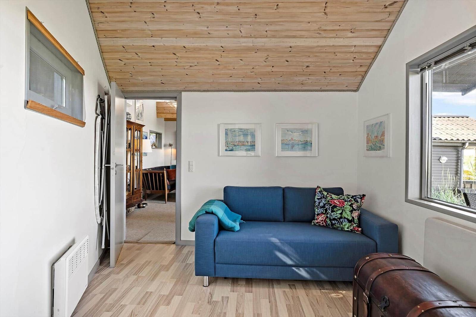 A room with a blue sofa, wooden floor, and wooden ceiling. Pictures hang on the wall.