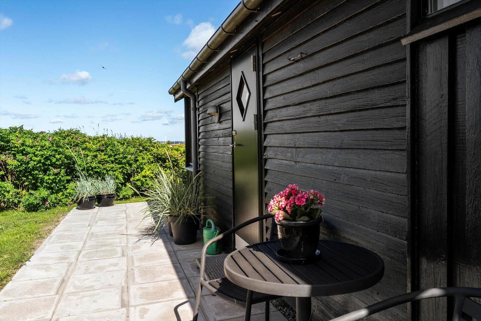 Terrace with table, chairs, and plants in front of a wooden house.
