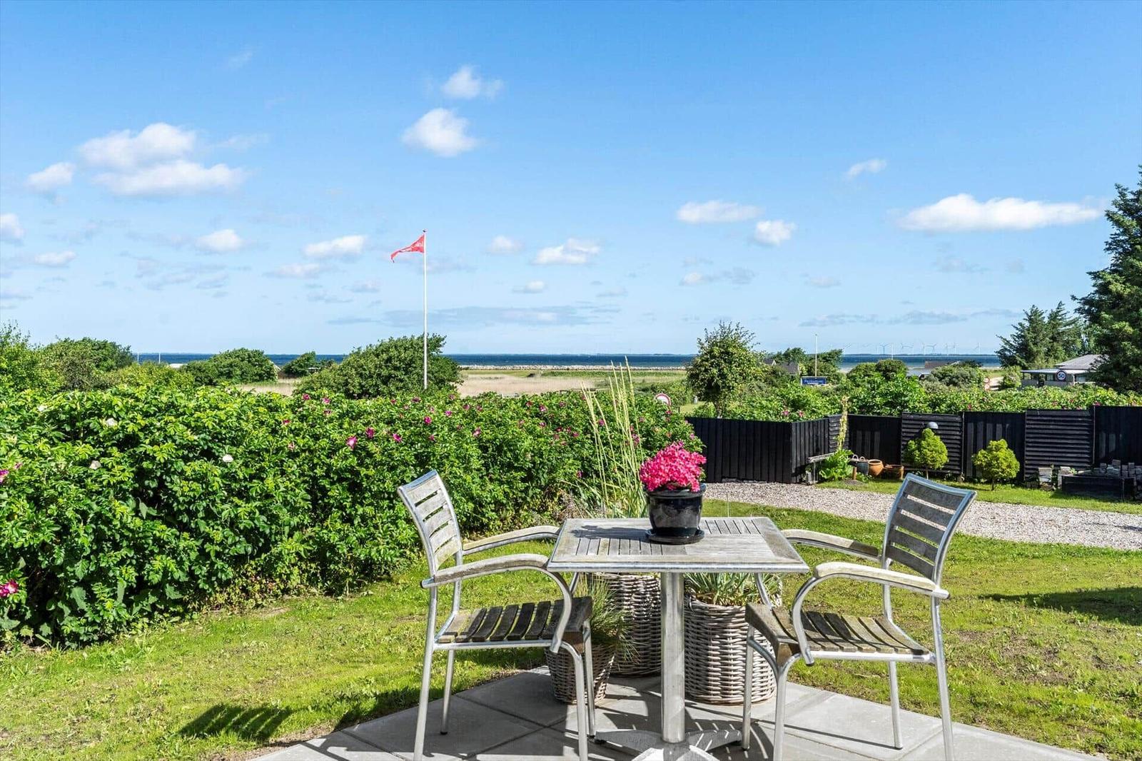 Terrace with table and chairs, view of green areas and sea under blue sky.