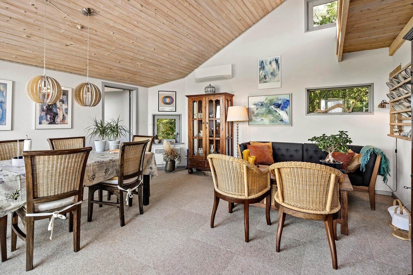 Dining area with table and chairs, living area with sofa and armchairs, wooden ceiling and wall art.