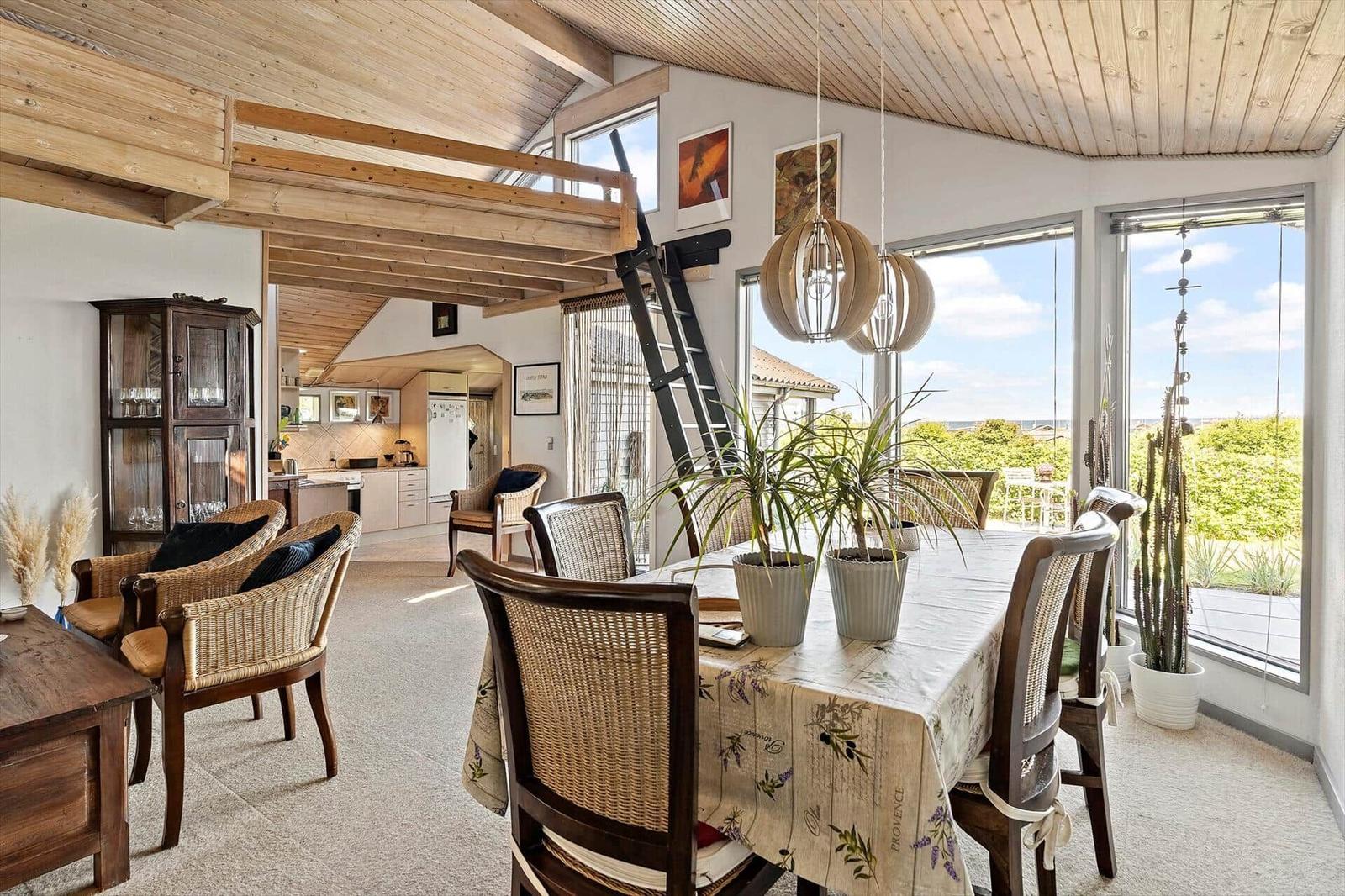 Dining room with table, chairs, and view of garden. Wooden ceiling and ladder to upper level.