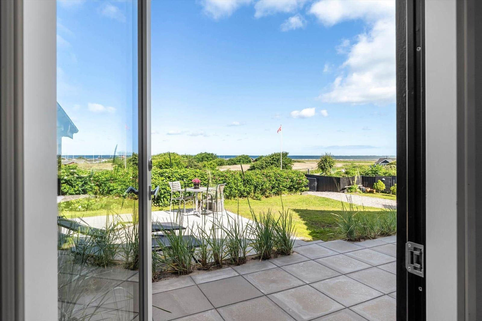Through the glass door, you see a terrace with garden and view of the sea.