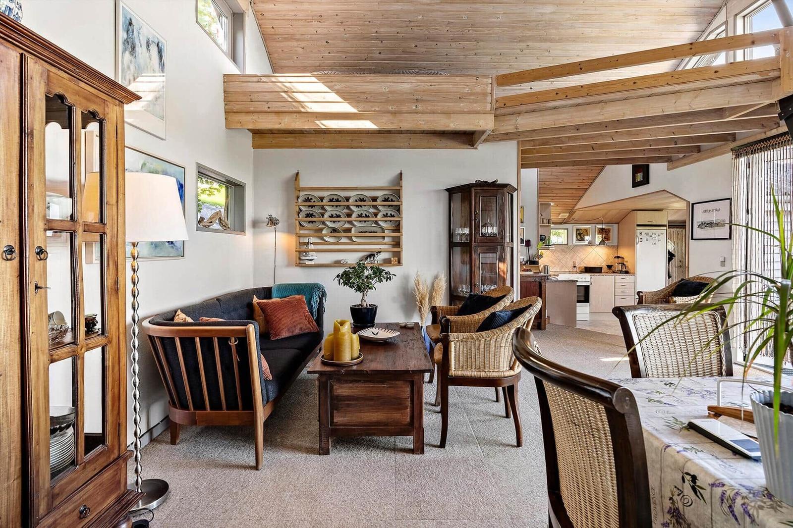 Living and dining area with wooden ceiling, sofa, table, and chairs. Kitchen visible in background.