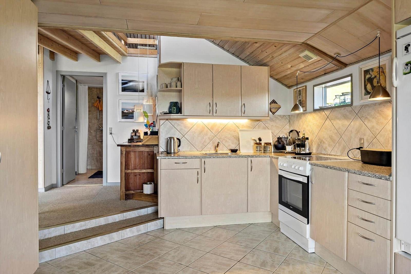 Kitchen with wooden ceiling, light cabinets, and white appliances. Passage to the bathtub.