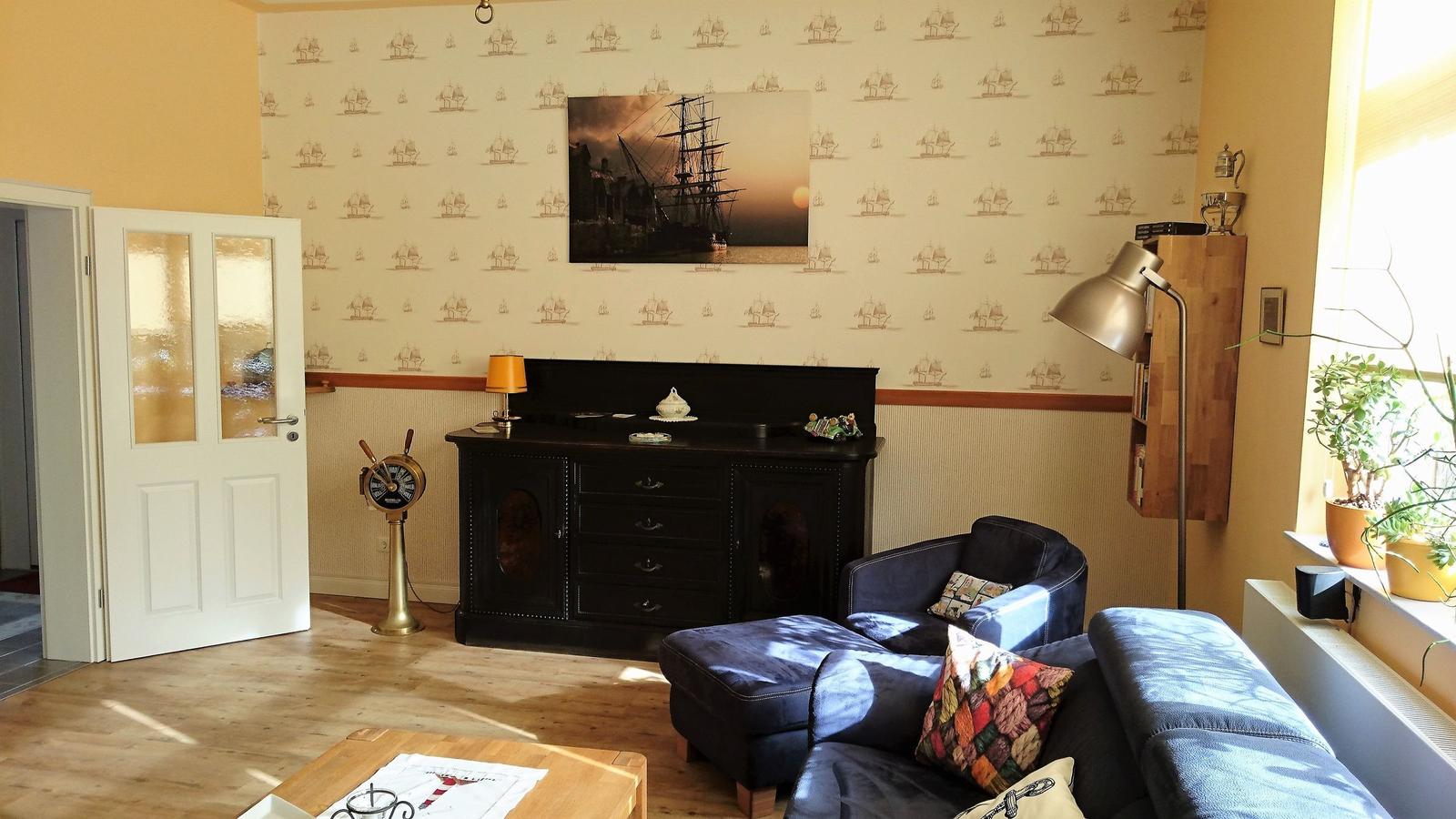 Wohnzimmer mit Sofa, Schrank und Wandtapete mit Schiffsmotiven.