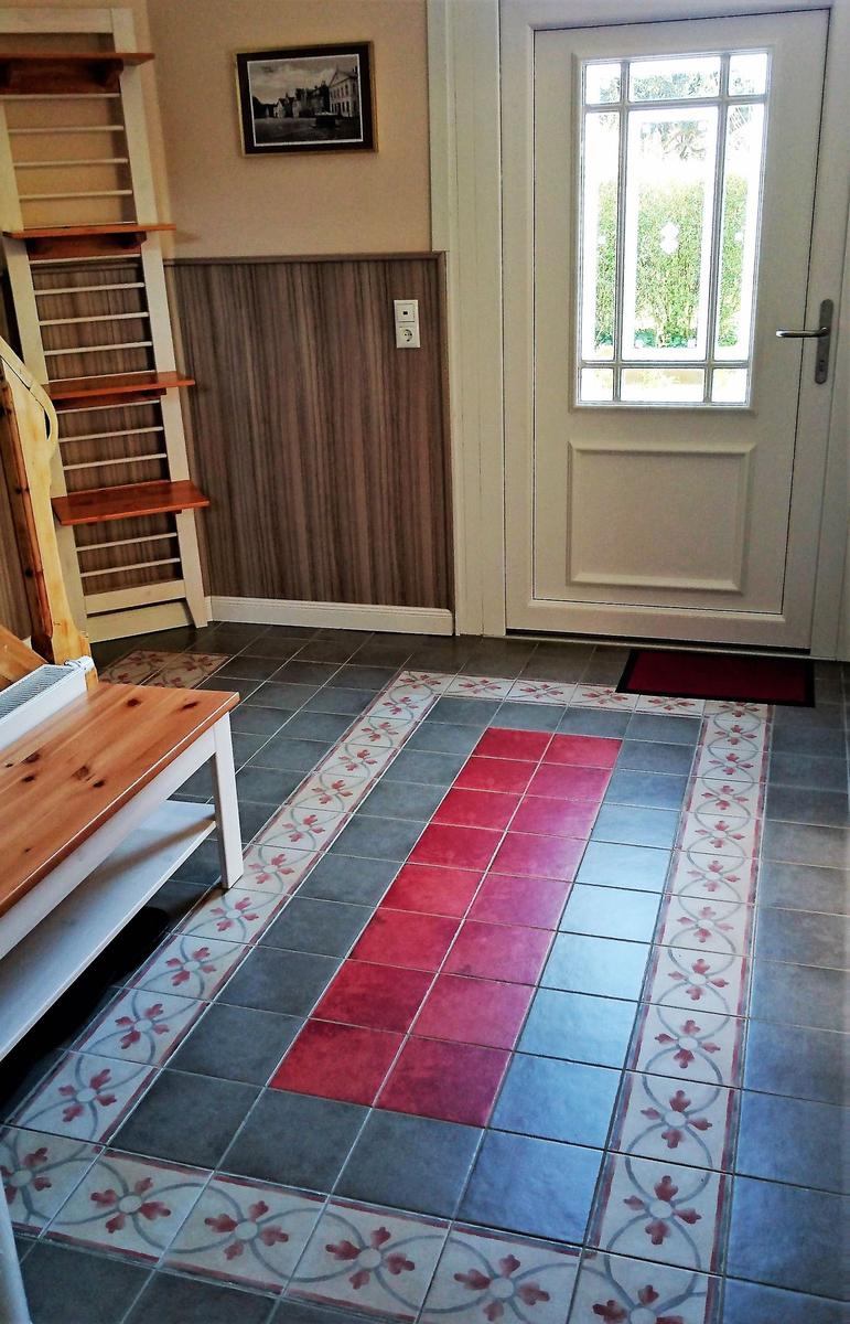 Eingangsbereich mit Holztreppe, Tür und gefliestem Boden mit Muster.