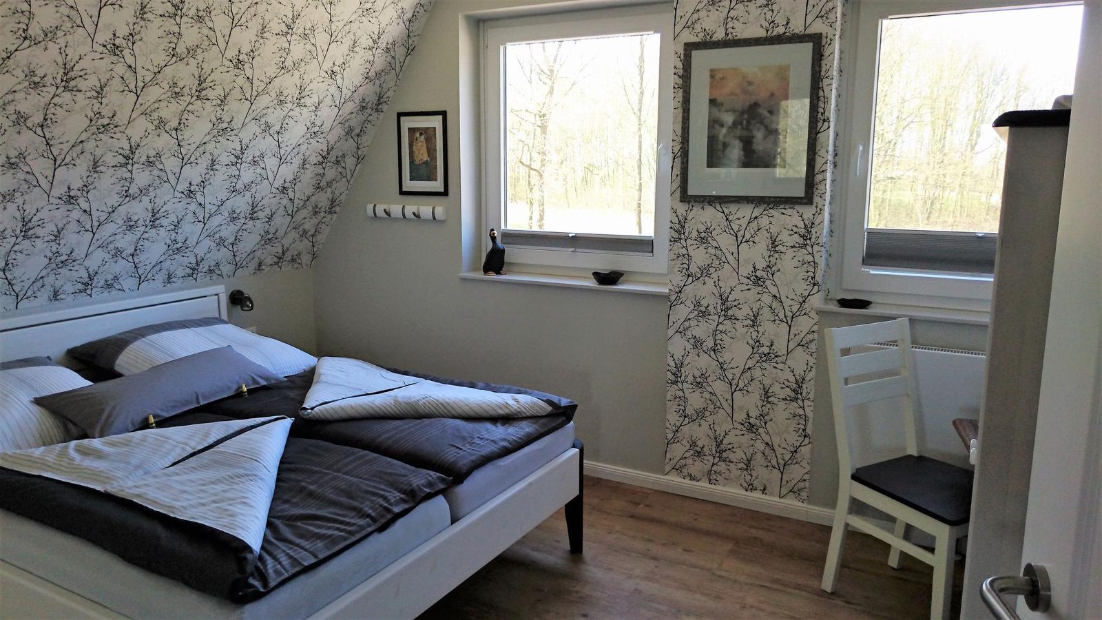 Schlafzimmer mit Bett, Fenstern und Tapete mit Baum-Motiv.