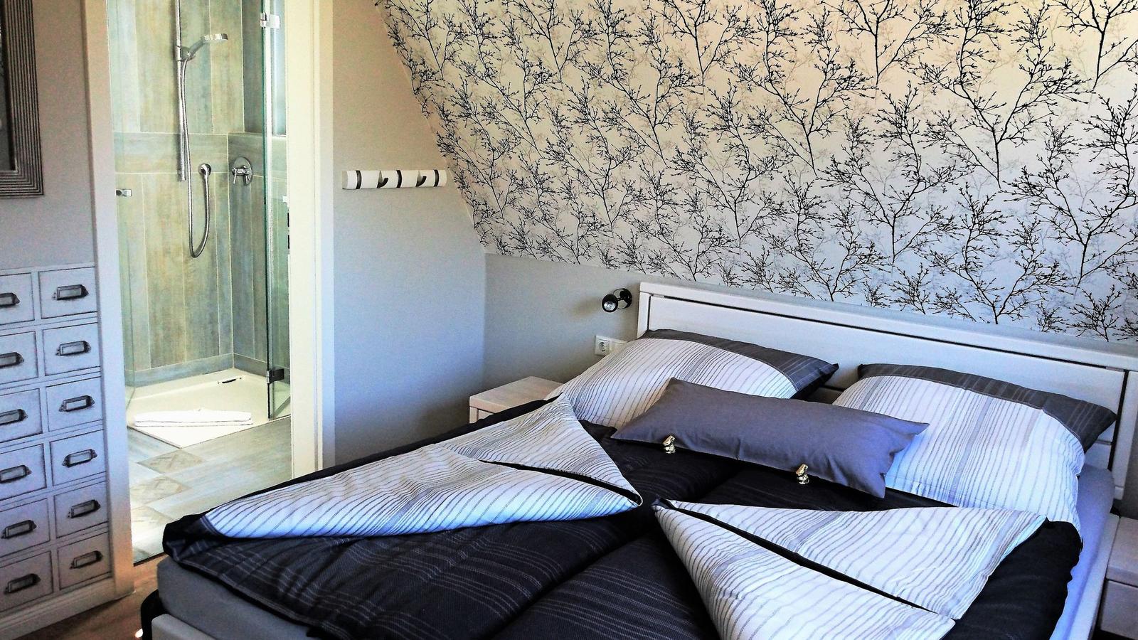 Schlafzimmer mit Doppelbett, Wand mit Baum-Motiv und angrenzender Dusche.
