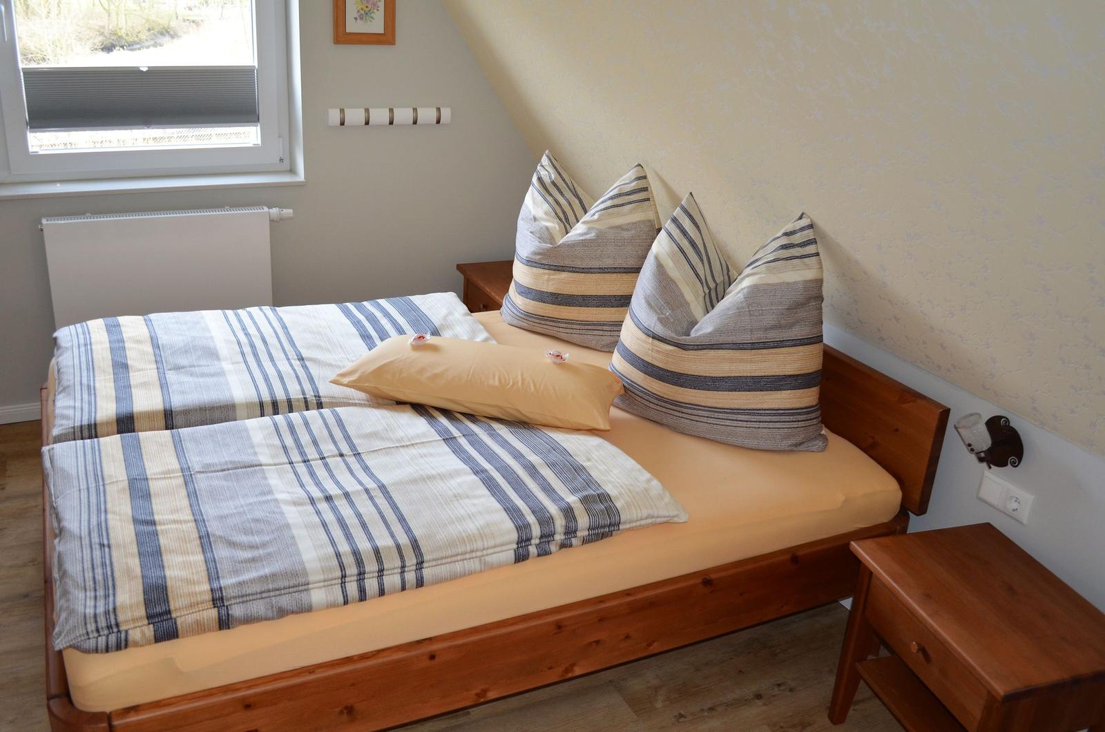 Schlafzimmer mit Doppelbett, Holzrahmen, Kissen und Fenster.