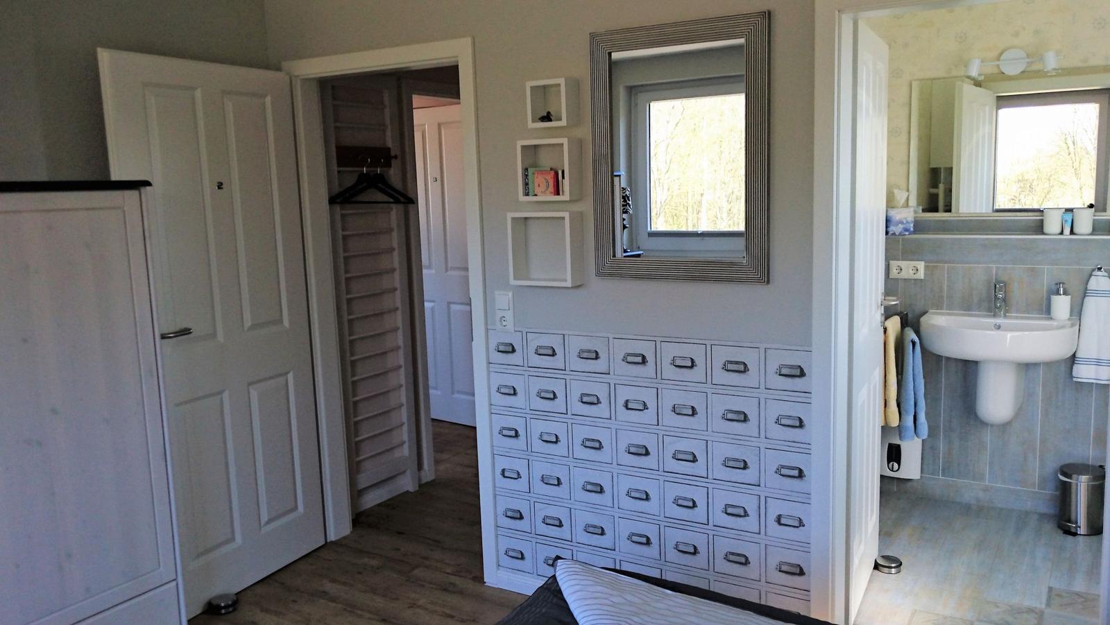 Schlafzimmer mit Kleiderschrank, Spiegelschrank und angrenzendem Bad mit Waschbecken.