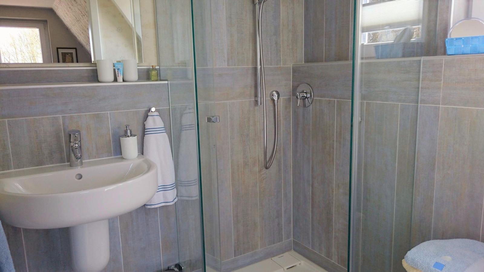 Badezimmer mit Dusche, Waschbecken und Spiegel.