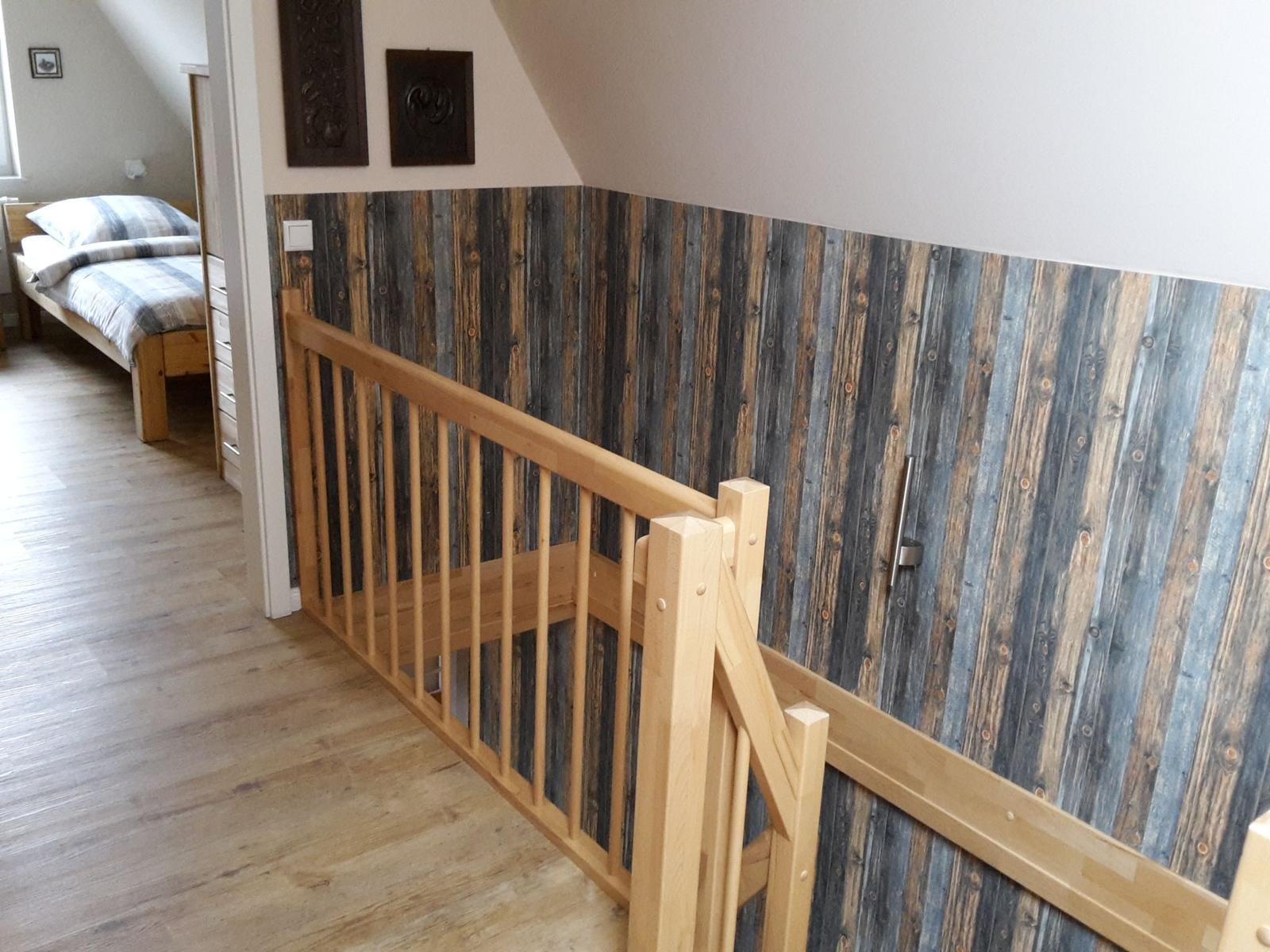Holzgeländer und rustikale Wandverkleidung im Flur mit Blick in Schlafzimmer.