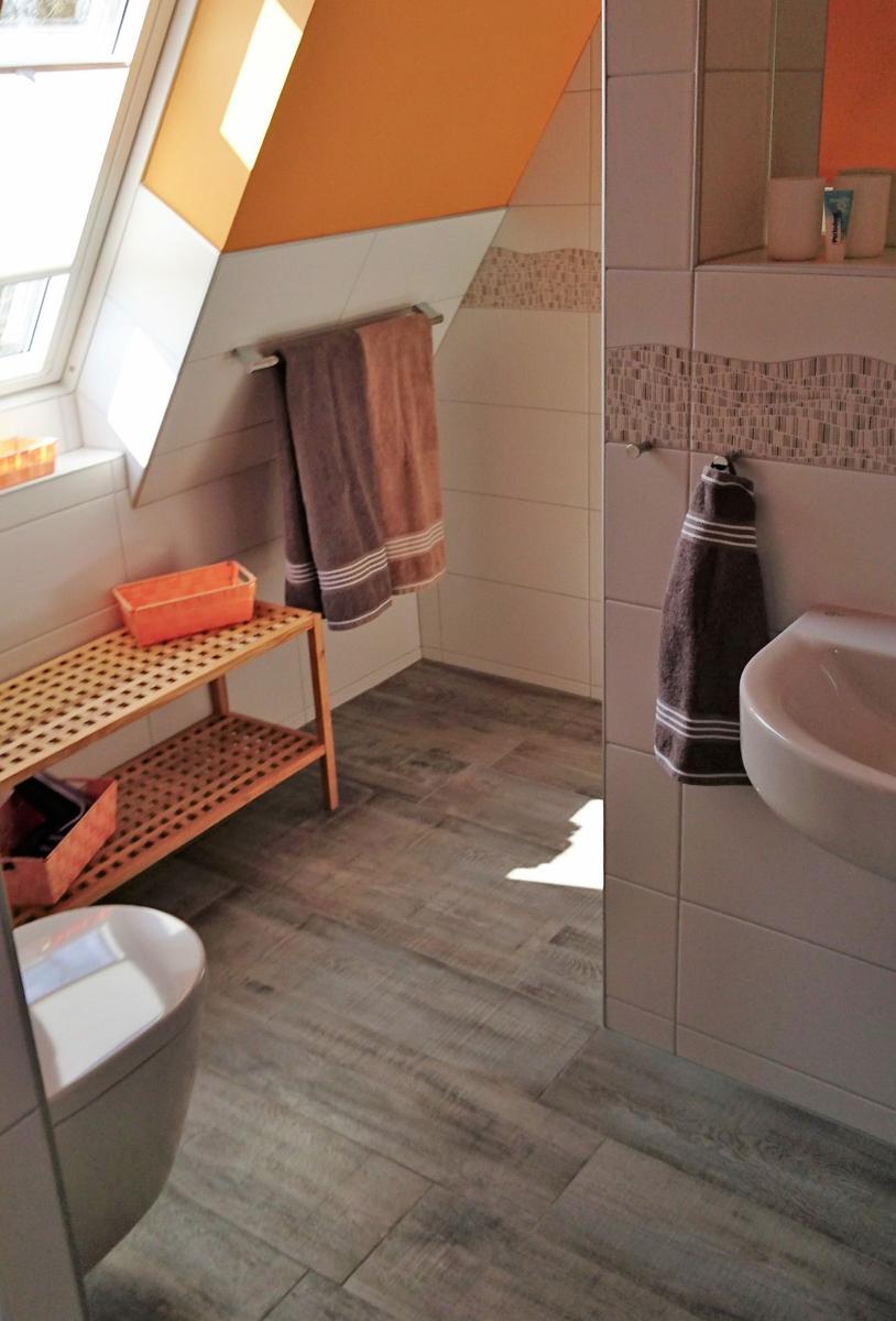 Badezimmer mit Dachschrägen, Toilette, Waschbecken und Holzregal.