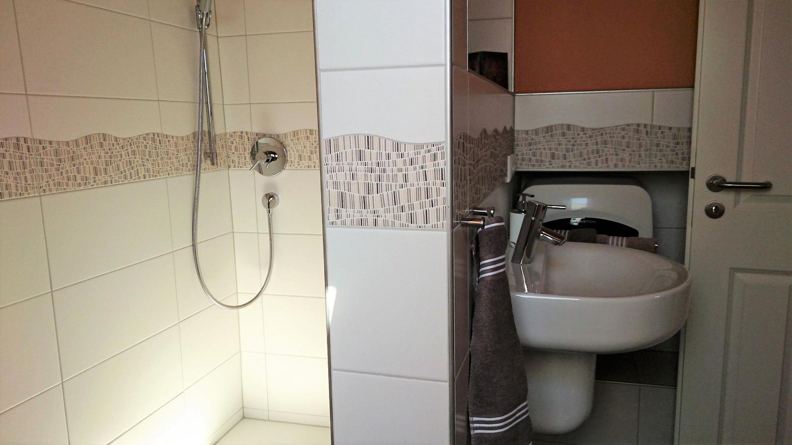 Badezimmer mit Dusche, Waschbecken und Toilette. Fliesen mit Mosaikverzierung.