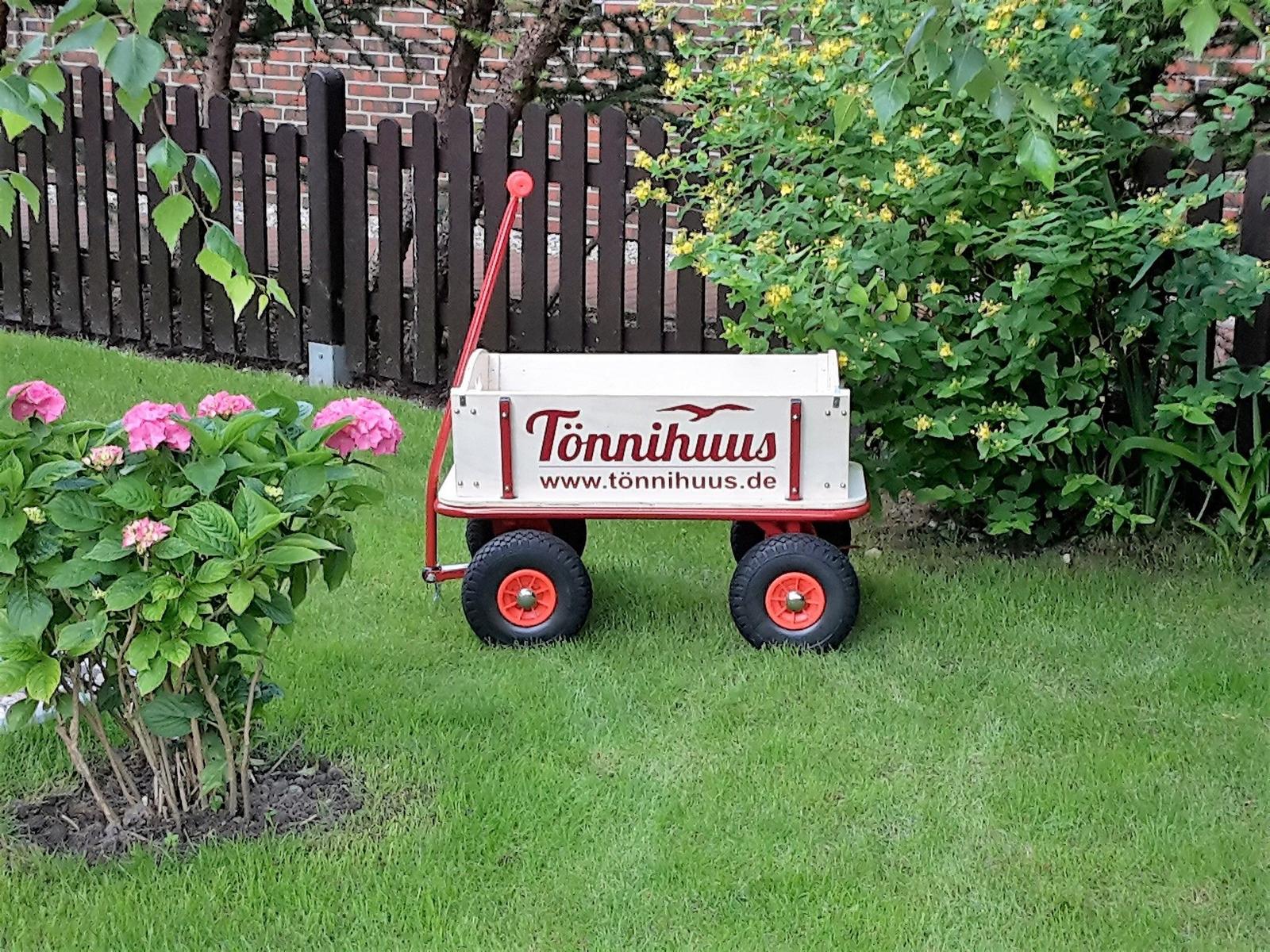 Ein roter Kinderwagen mit weißem Kasten steht auf einer grünen Wiese.