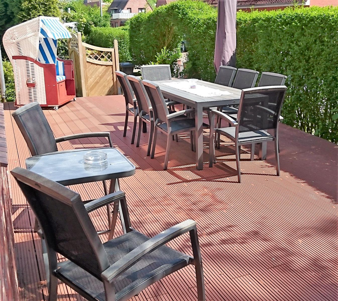 Terrasse mit Tisch, Stühlen und Liegestuhl. Holzdecke und grüne Hecke im Hintergrund.