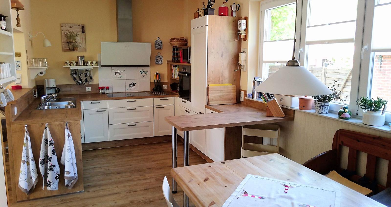 Küche mit Holzoberflächen, weißen Schränken und Fenster mit Pflanzen