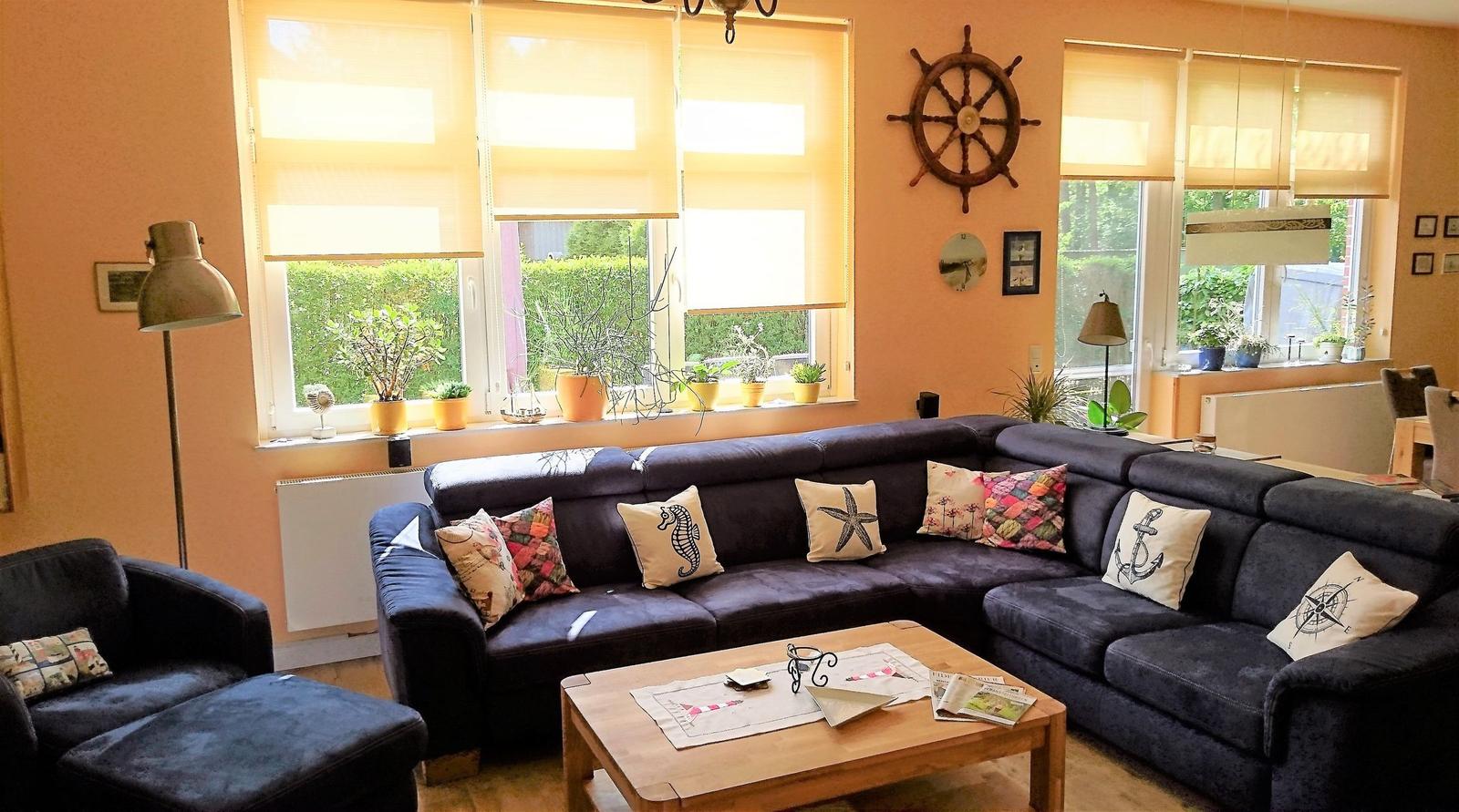 Wohnzimmer mit dunklem Sofa, dekorativen Kissen und Holztisch. An den Wänden hängen ein Ruder und Bilder.