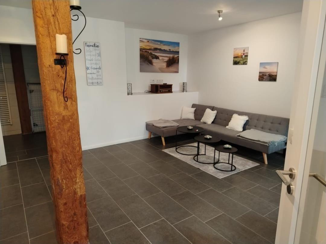 Wohnzimmer mit grauem Sofa, drei runden Tischen und Wandbildern.