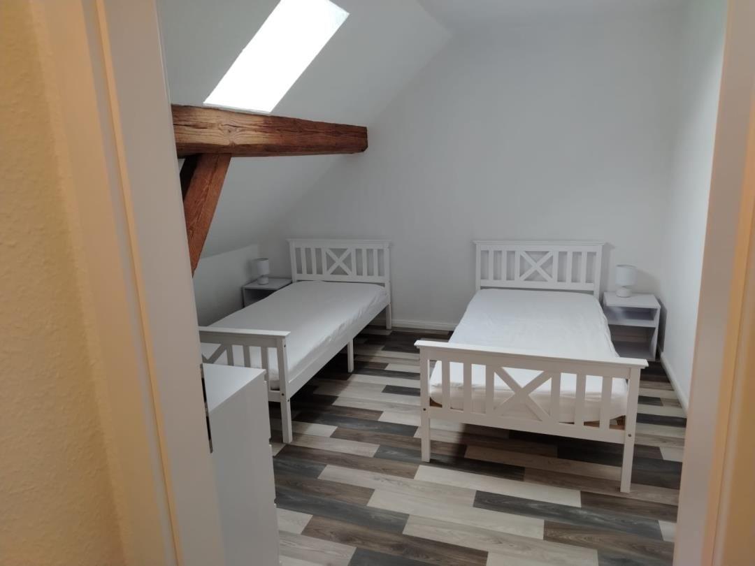 Zwei weiße Einzelbetten mit Nachttischen unter Dachschrägen und Holzbalken.