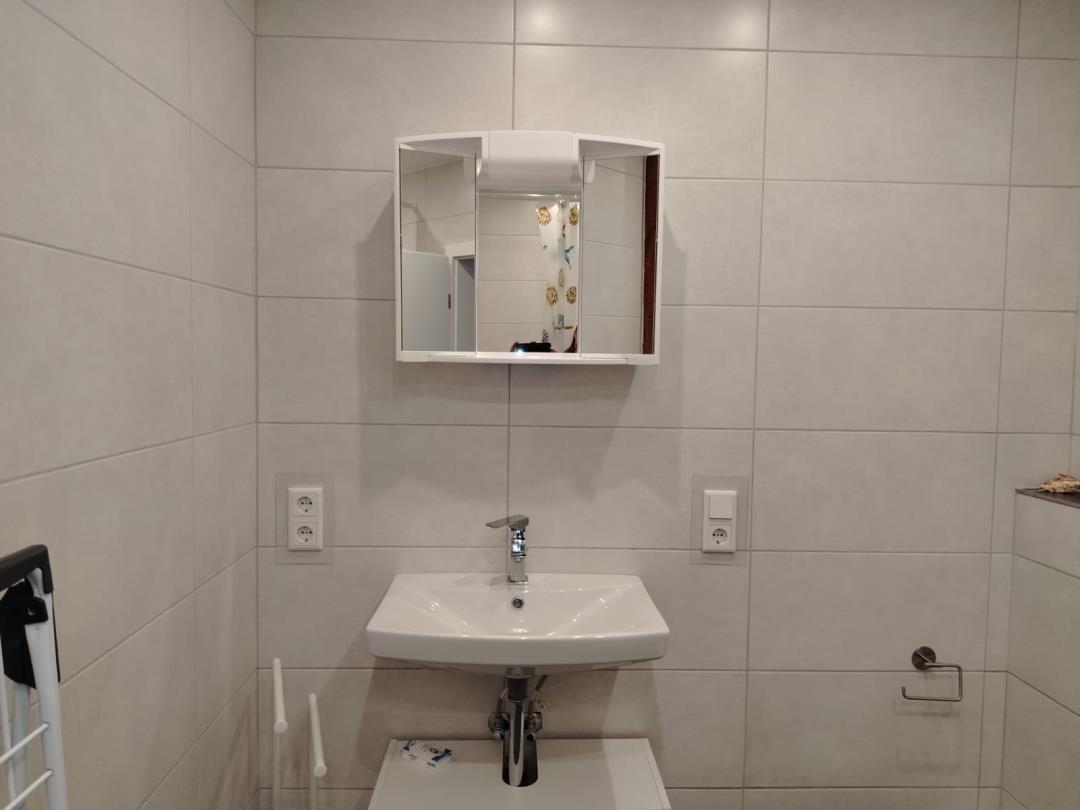 Badezimmer mit Waschbecken, Spiegelschrank und Toilettenpapierhalter.