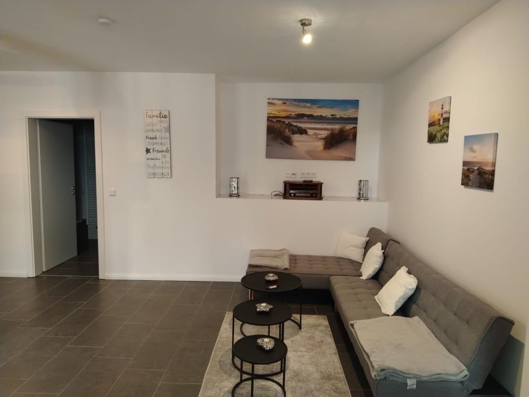 Wohnzimmer mit grauem Sofa, drei runden Tischen und Wandbildern.
