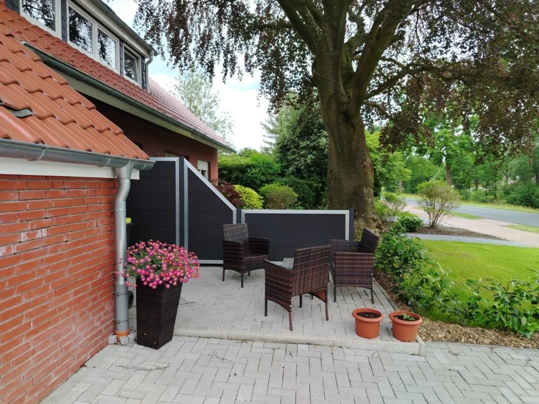 Terrasse mit Sitzgruppe, Blumenkübel und Blick auf einen Baum und Rasen.