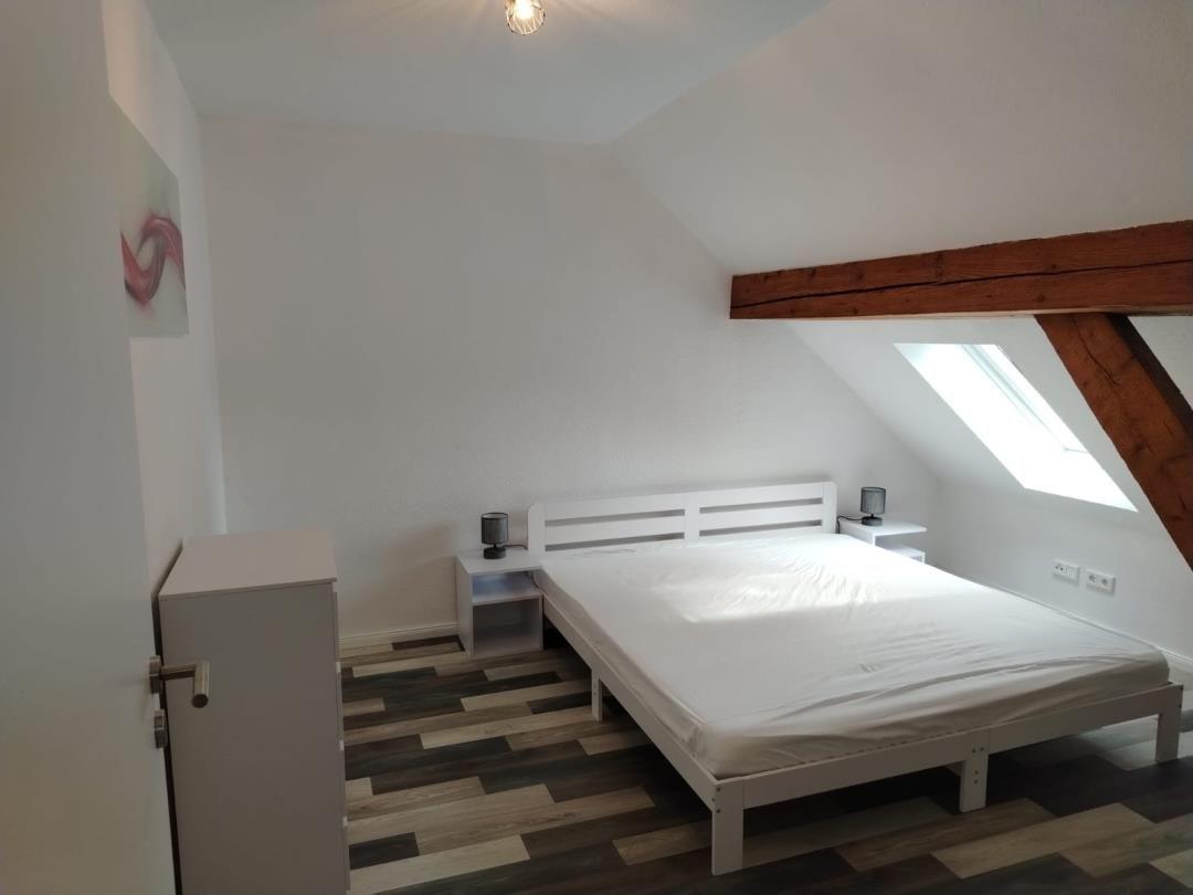 Schlafzimmer mit Dachschrägen, weißem Bett und Holzboden. Dachfenster und Holzbalken sichtbar.