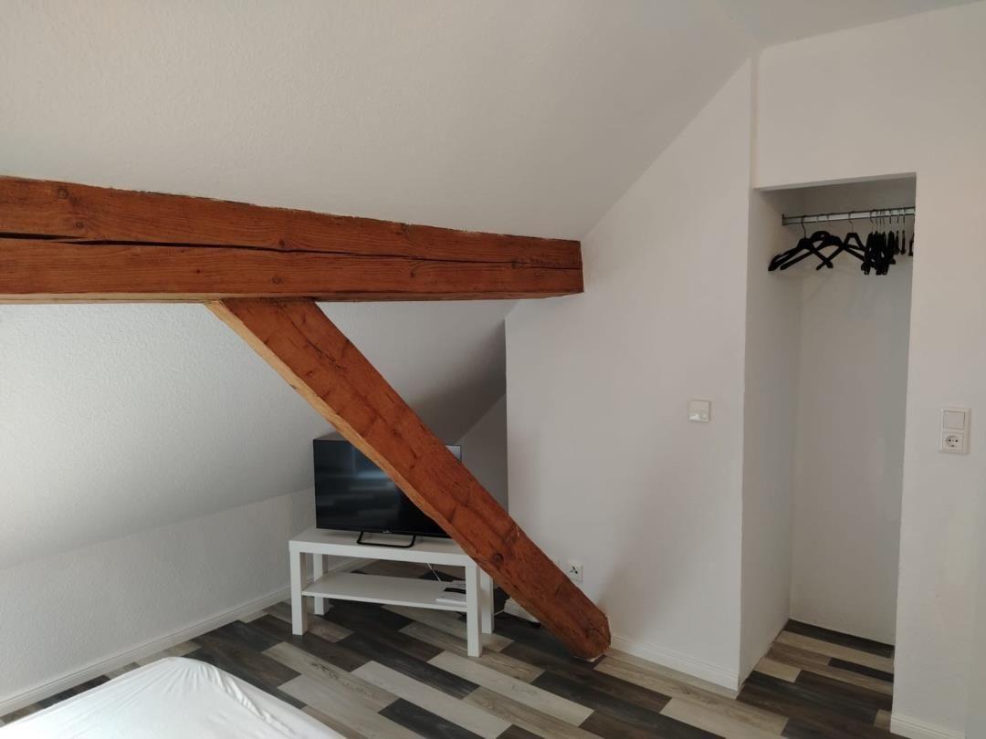 Schlafzimmer mit Holzbalken, Kleiderschrank und TV-Ständer.