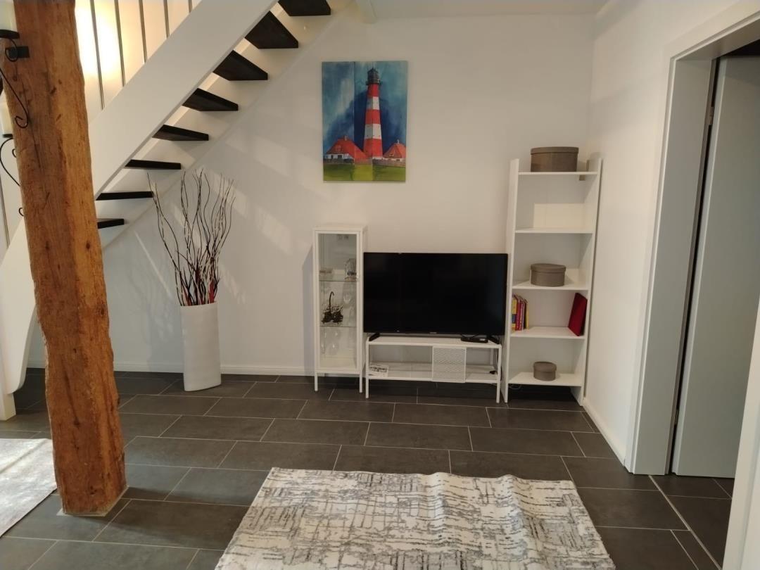 Wohnzimmer mit Fernseher, Regal und Treppe. Wandbild zeigt Leuchtturm.