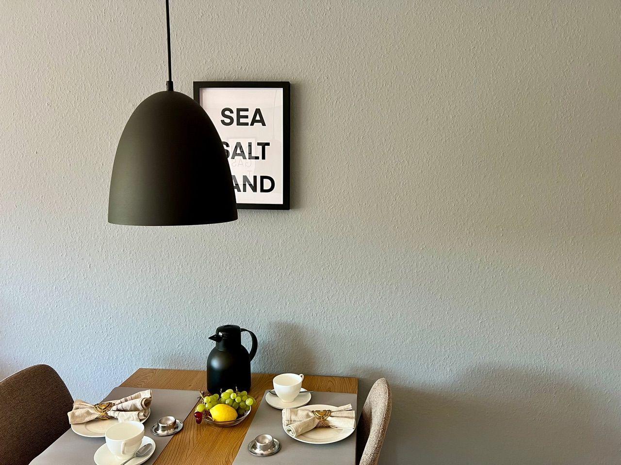 Esstisch mit zwei Plätzen, schwarzer Hängelampe und Bild an der Wand.