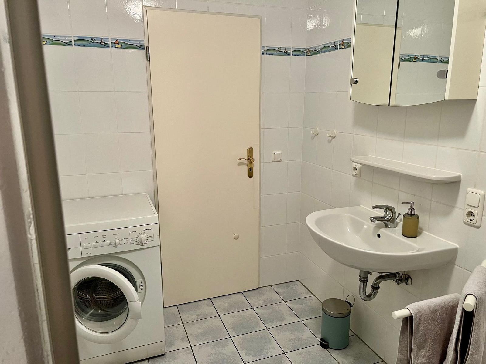Badezimmer mit Waschmaschine, Waschbecken und Spiegel