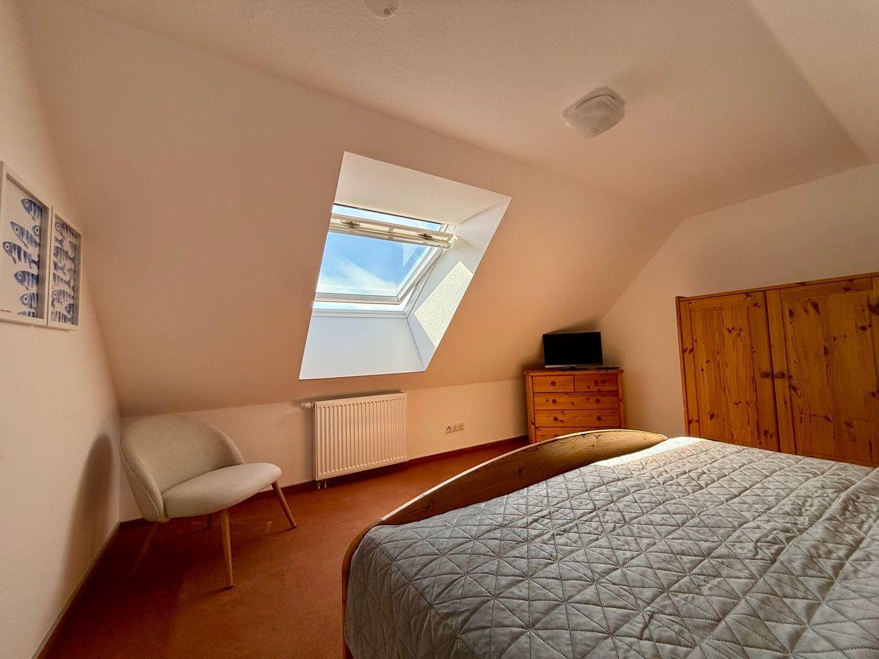 Schlafzimmer mit Dachschräge, Dachfenster, Bett, Kleiderschrank und Stuhl.