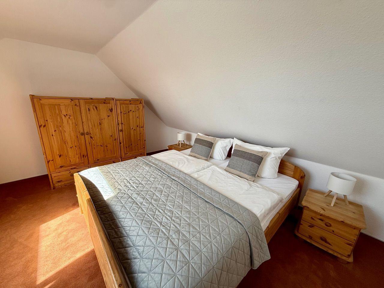 Schlafzimmer mit Holzbett, Nachttischen und Kleiderschrank unter Dachschrägen.