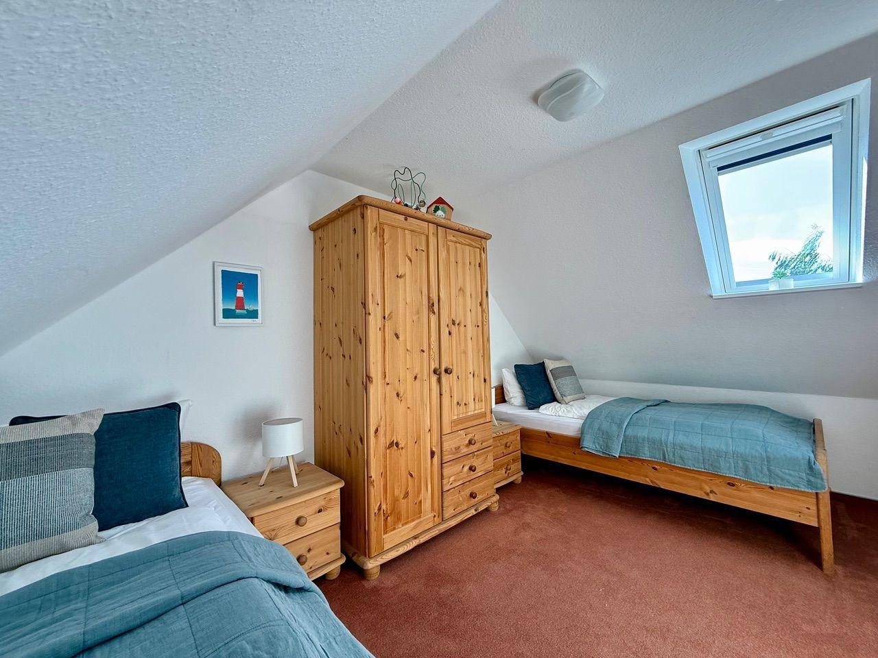 Zimmer mit zwei Betten, Holzschrank und Dachfenster.