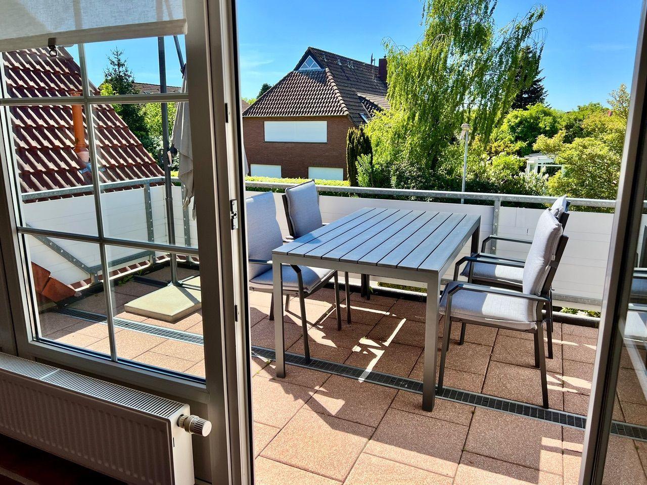 Terrasse mit Tisch und Stühlen, Blick auf Grün und Dächer.