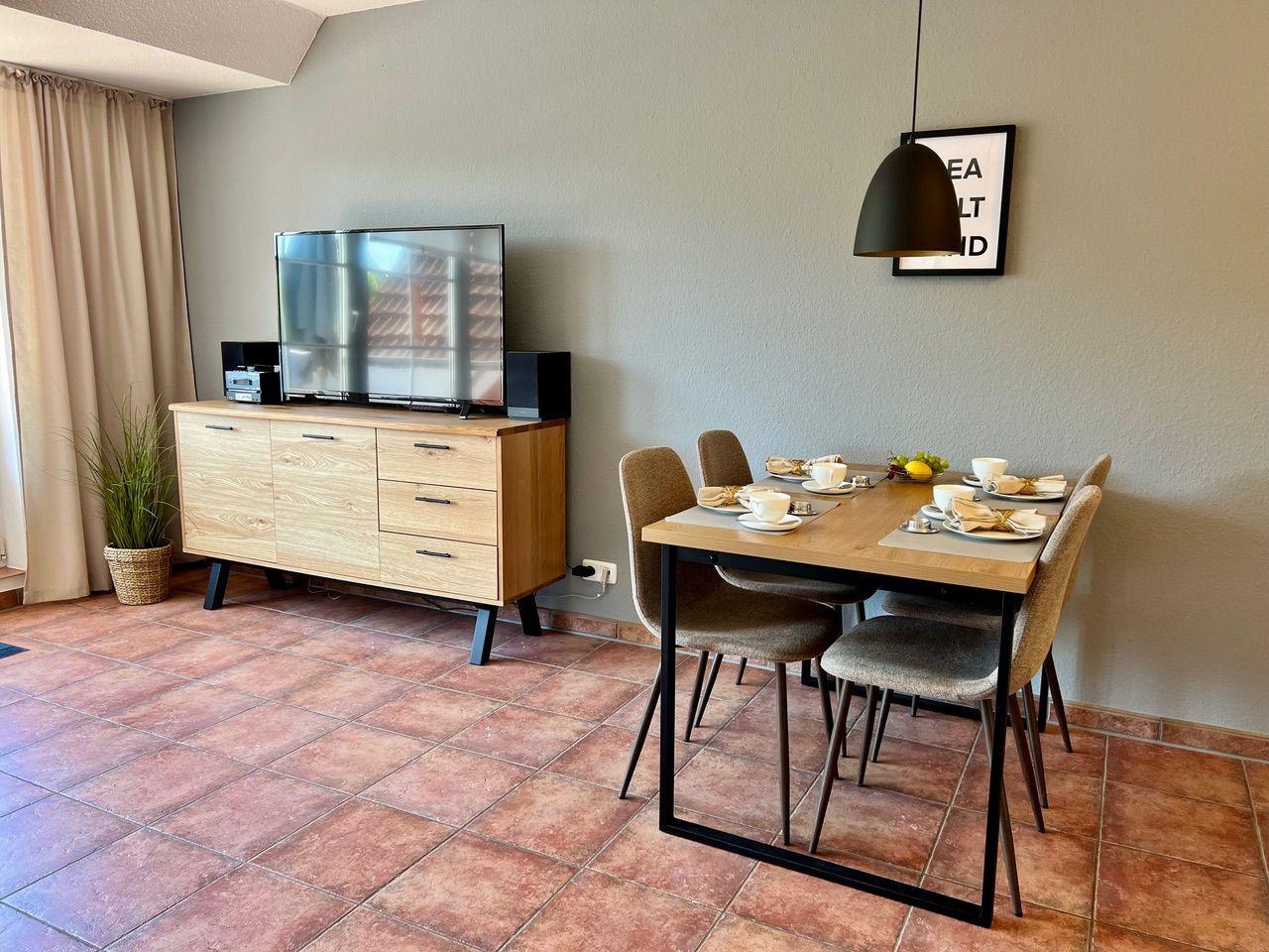Esszimmer mit Tisch, Stühlen und TV-Schrank. Terrakottafußboden und Wandbild.