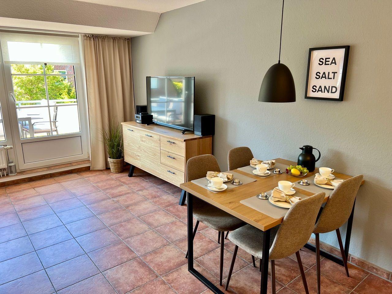 Essbereich mit Tisch, Stühlen und TV. Fenster zur Terrasse. Wandbild: SEA SALT SAND.