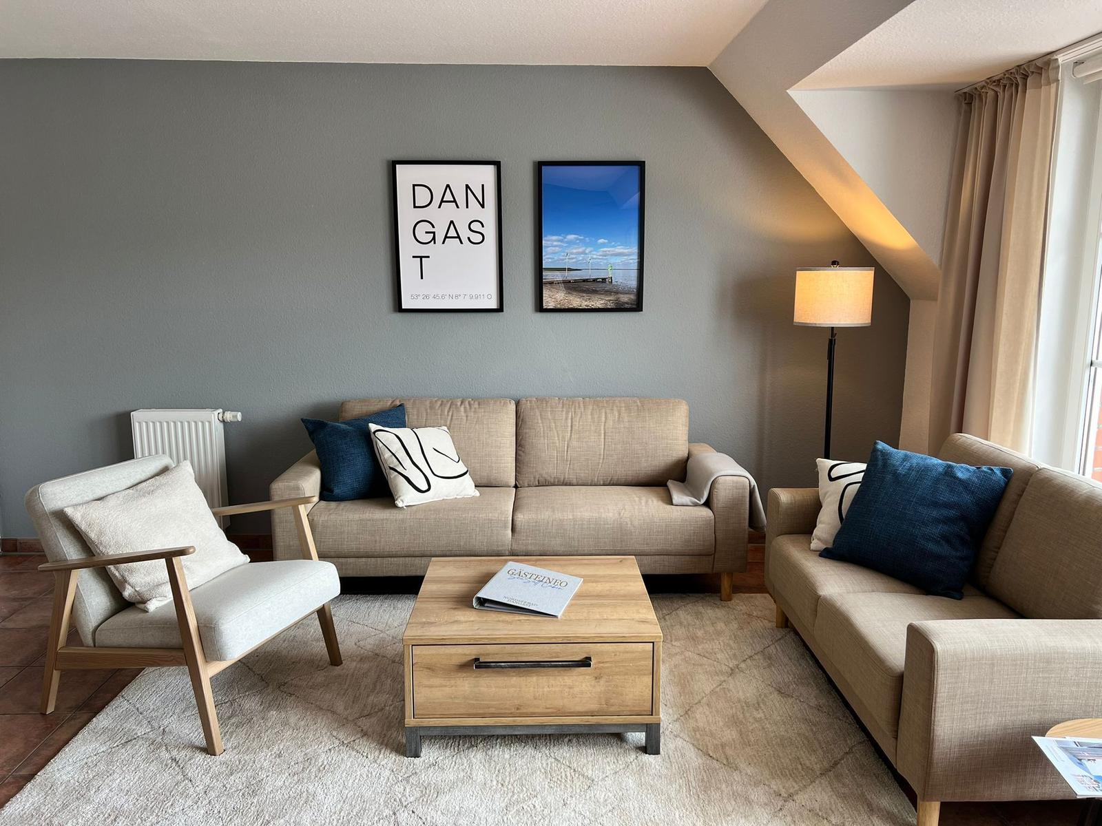 Wohnzimmer mit Sofa, Sessel, Couchtisch und Wandbildern.