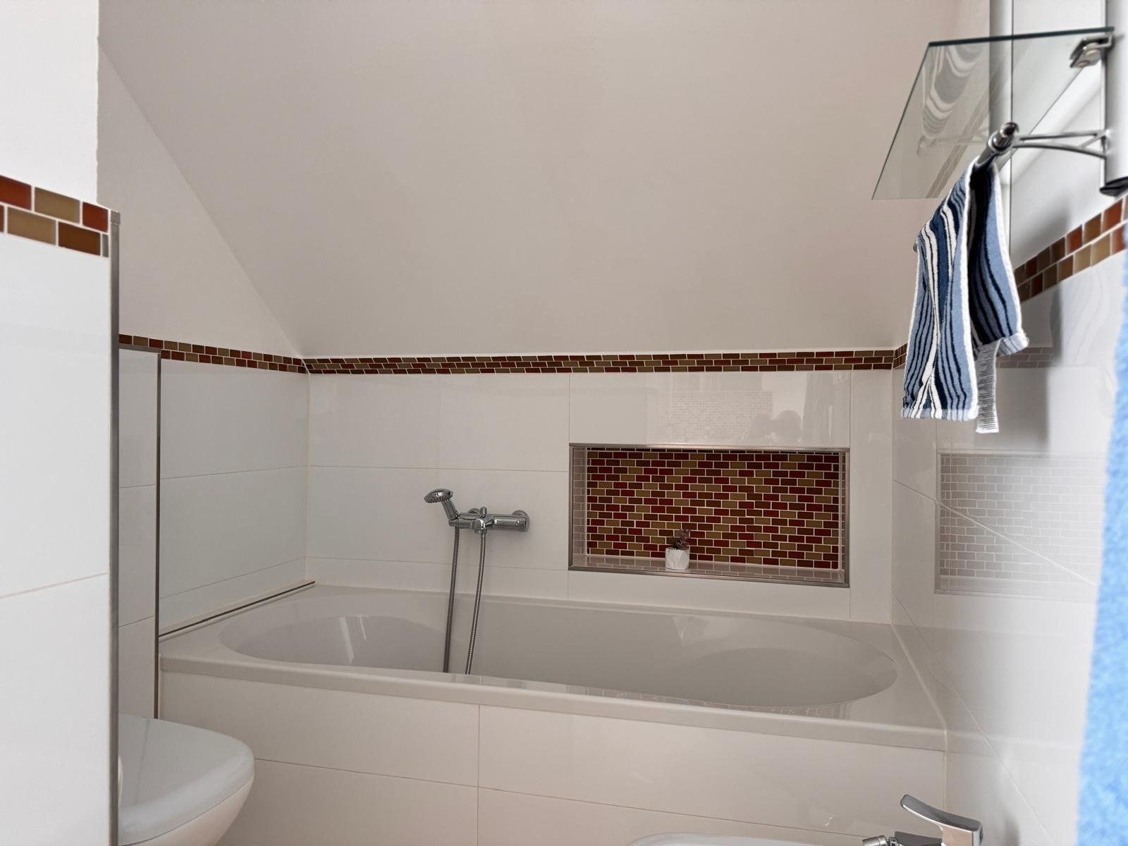 Badezimmer mit Badewanne, Duschwand und Mosaikfliesen an der Wand.