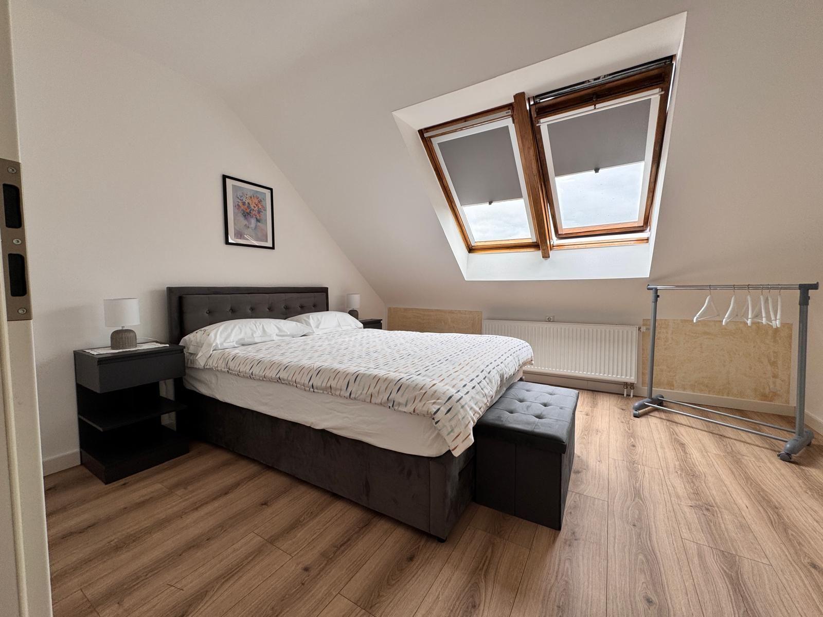Schlafzimmer mit Dachschräge, Doppelfenster und Holzboden.
