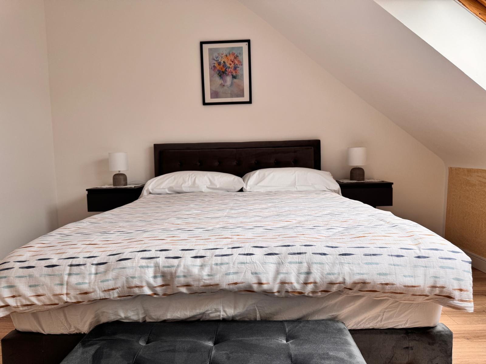 Schlafzimmer mit Doppelbett, Nachttischen und Wandbild unter Dachschrägen.