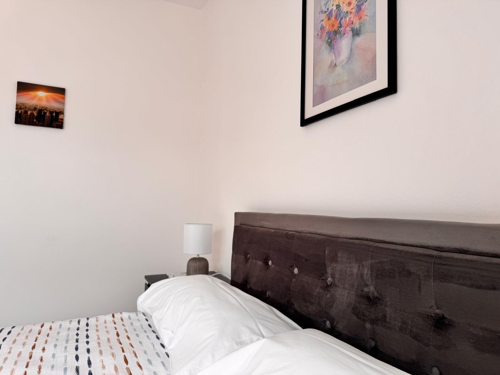 Schlafzimmer mit Bett, Nachttisch und Wandbildern.