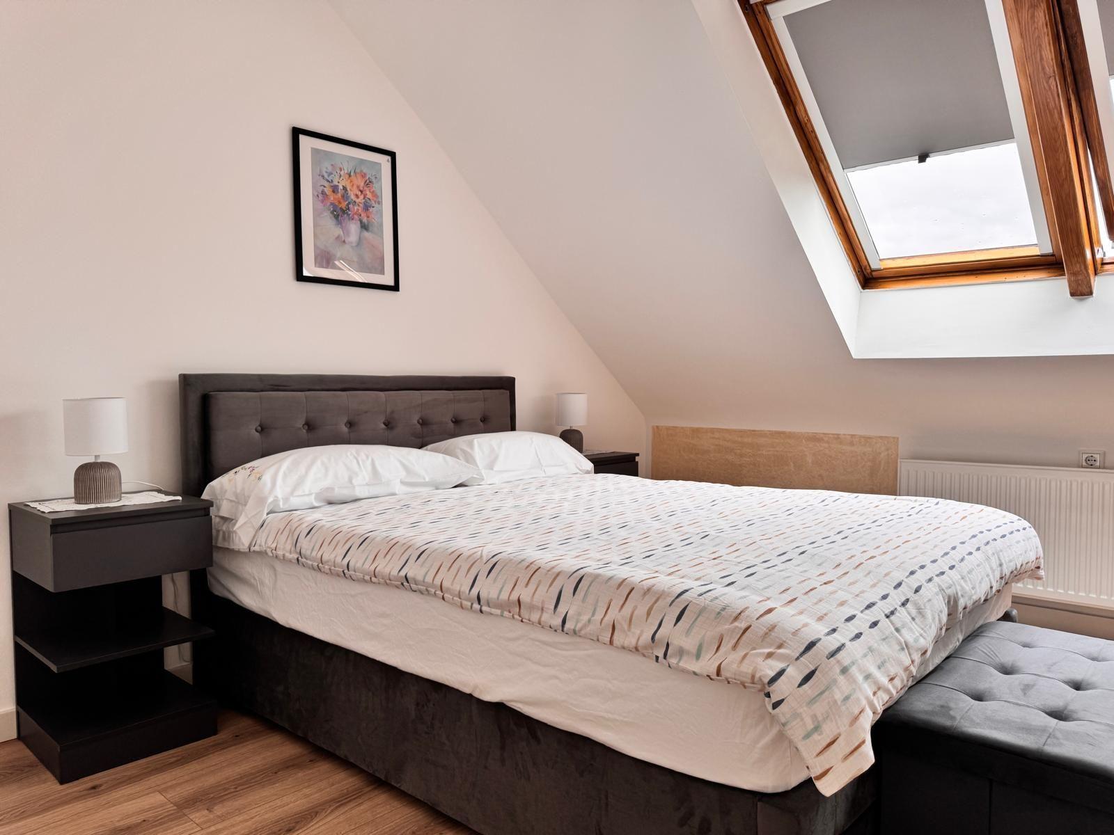 Schlafzimmer mit Dachschrägen, Doppelbett, Nachttischen und Dachfenster.