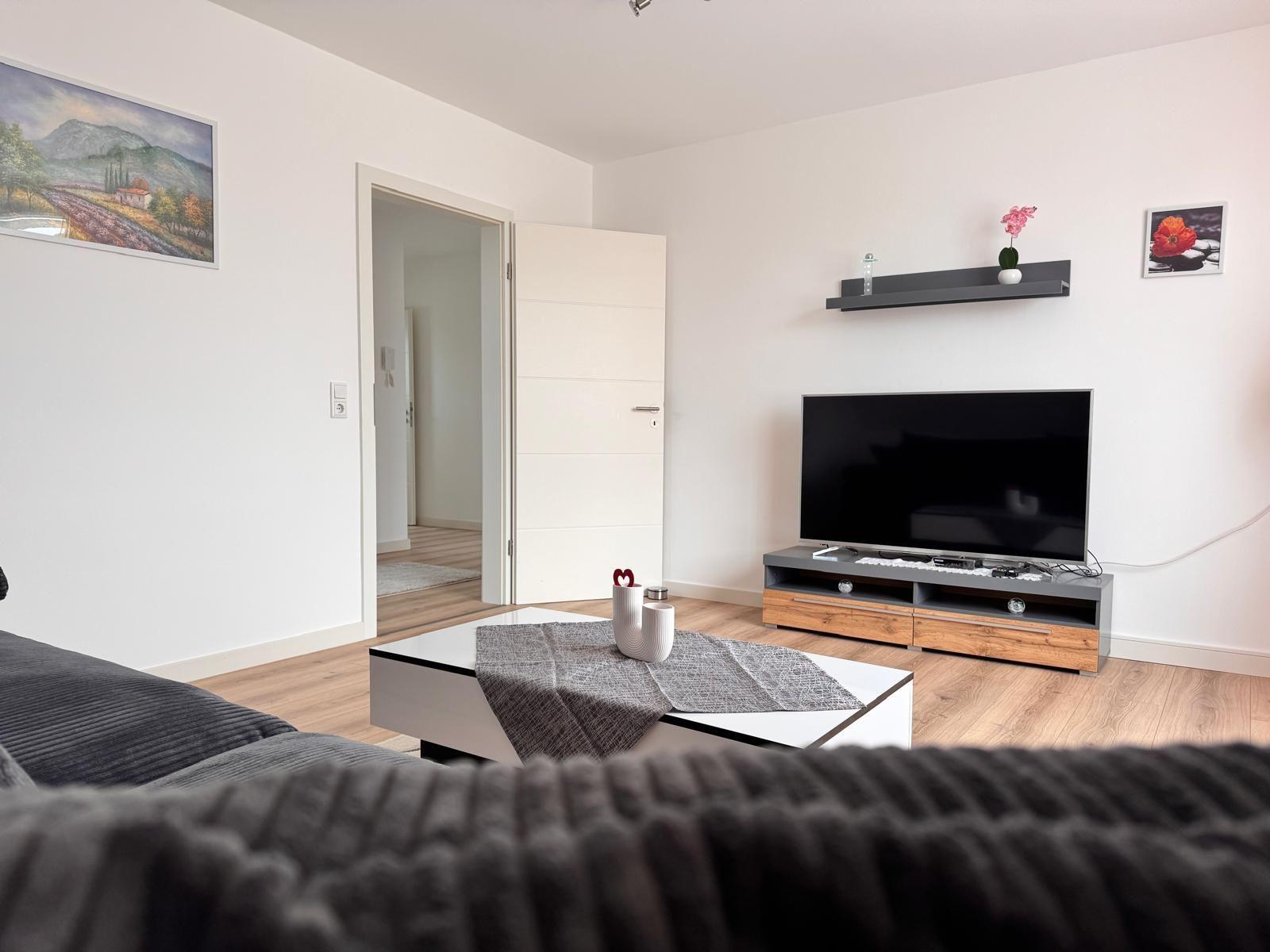 Wohnzimmer mit Fernseher, Couch und Tisch. Wandbild und Schrank sichtbar.
