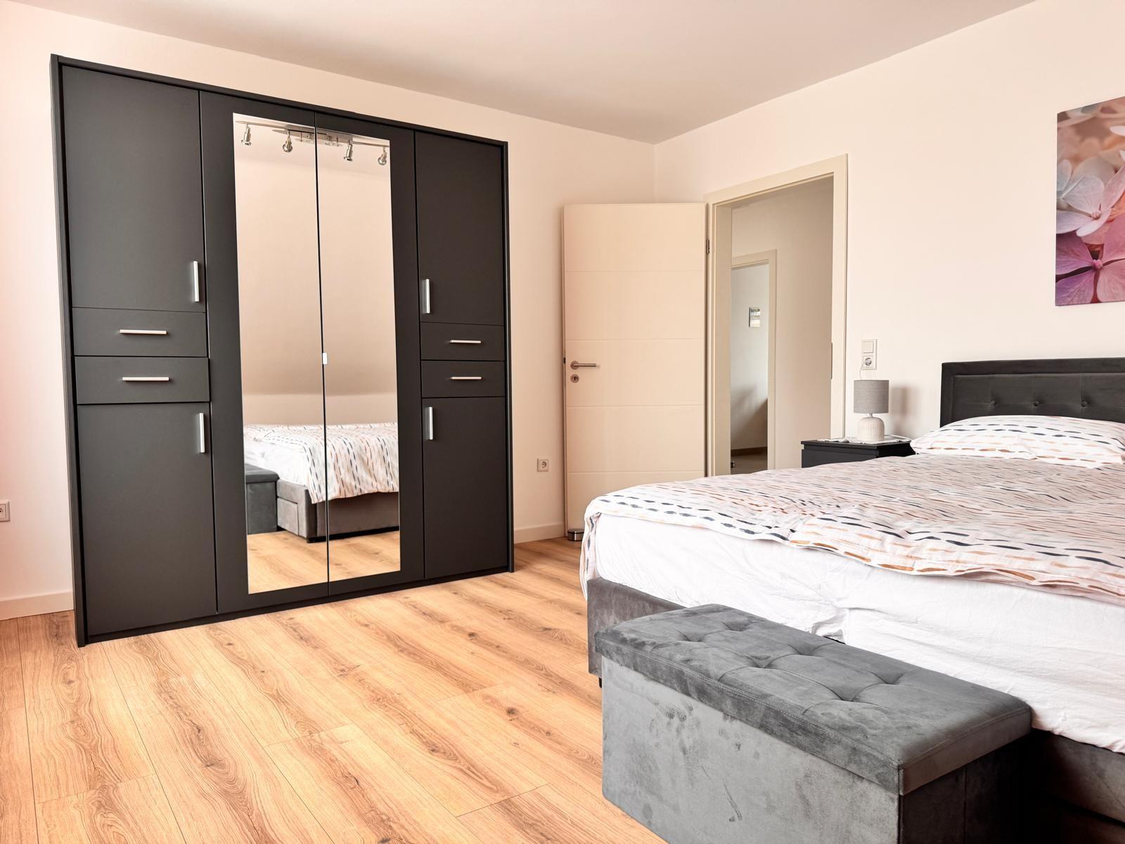 Schlafzimmer mit Bett, Kleiderschrank und Fußbank.